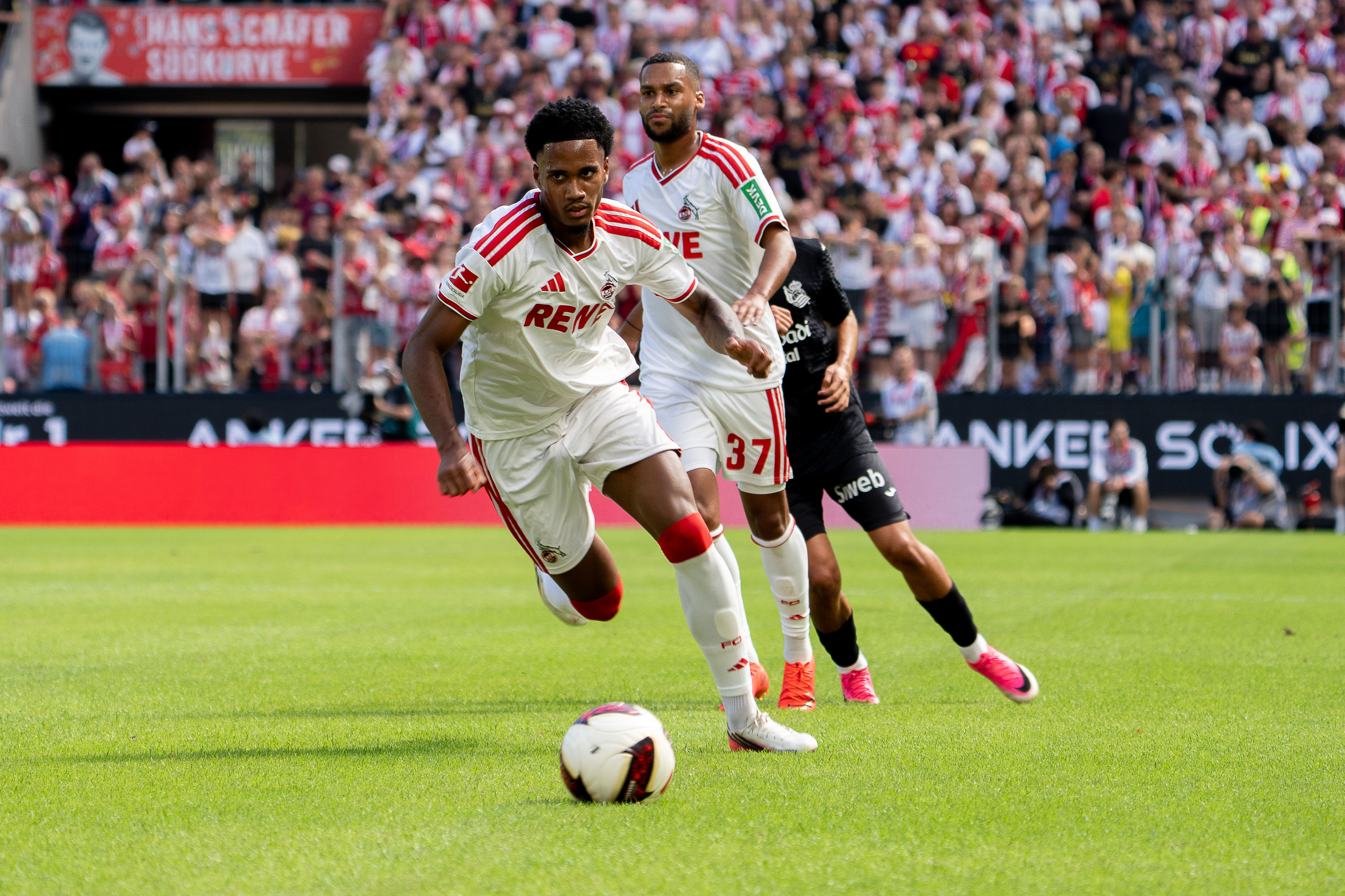 Jahmai Simpson-Pusey (#22; 1. FC Köln) im Dribbling, Linton Maina (#37; 1. FC Köln) in Laufbewegung, Gegner in schwarzem Trikot, Freundschaftsspiel 1. FC Köln – Real Sociedad.
Foto: Alexander Franz