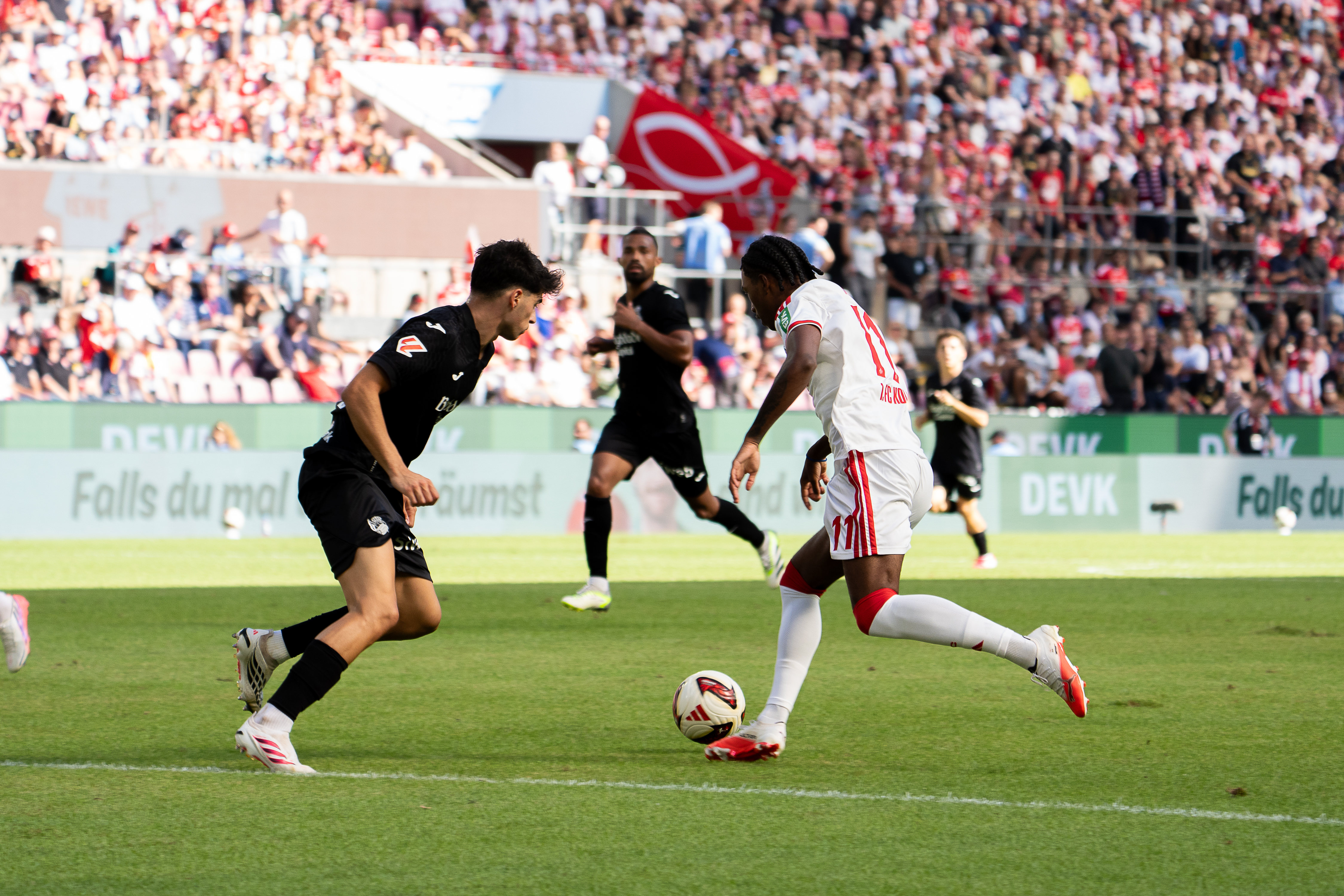 Jahmai Simpson-Pusey (#22; 1. FC Köln) mit Ball am Fuß im Zweikampf gegen einen Spieler von Real Sociedad in schwarzem Trikot beim Freundschaftsspiel 1. FC Köln gegen Real Sociedad.
Foto: Alexander Franz