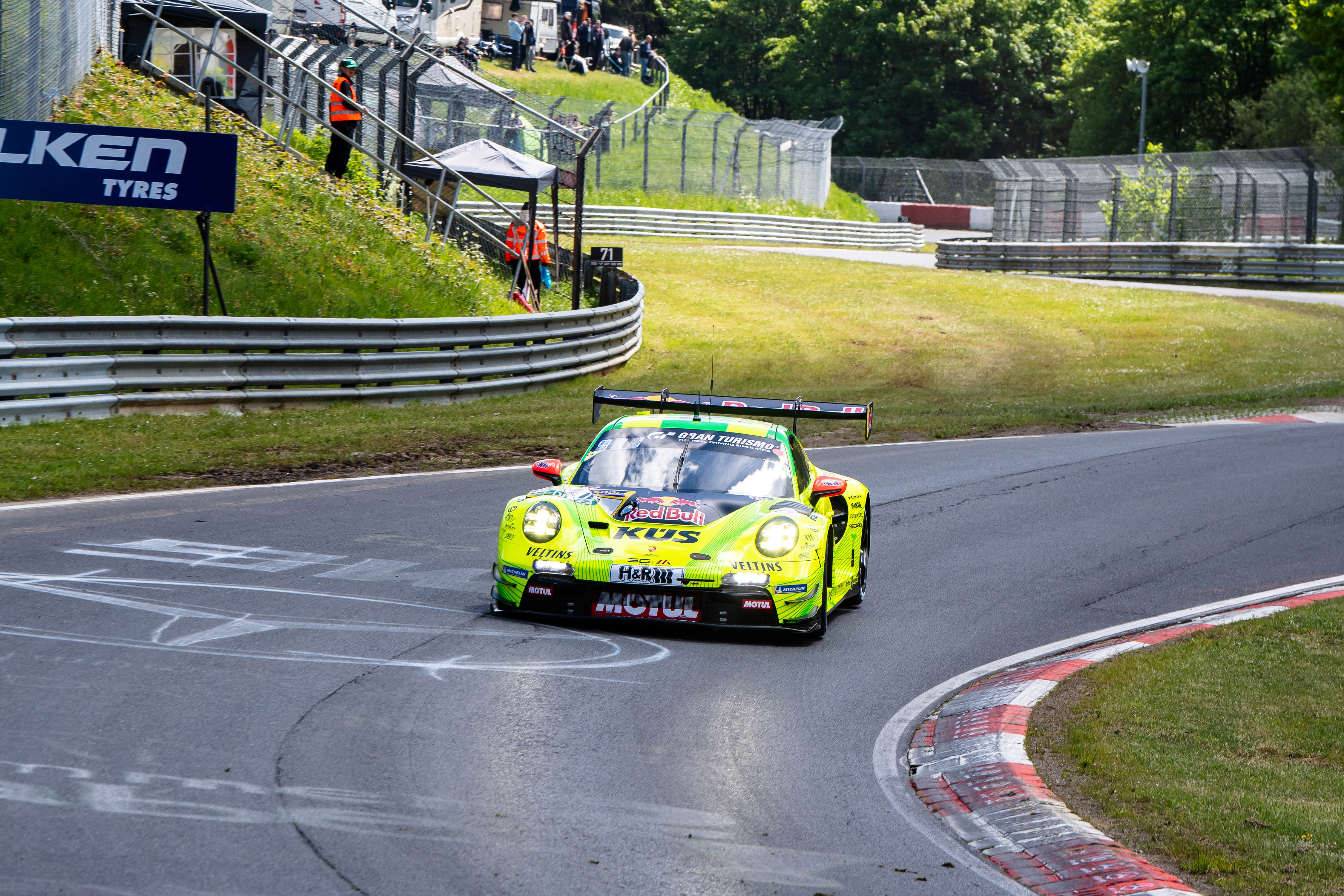Manthey SP 9 PRO (IGTC) (#911) mit den Fahrern Kevin Estre (FRA), Ayhancan Güven (TUR), Thomas Preining (AUT). Ein gelb-grün lackierter Manthey Porsche (#911) fährt eine Kurve auf der Rennstrecke während des ADAC RAVENOL 24h Nürburgring GE Qualifying 1