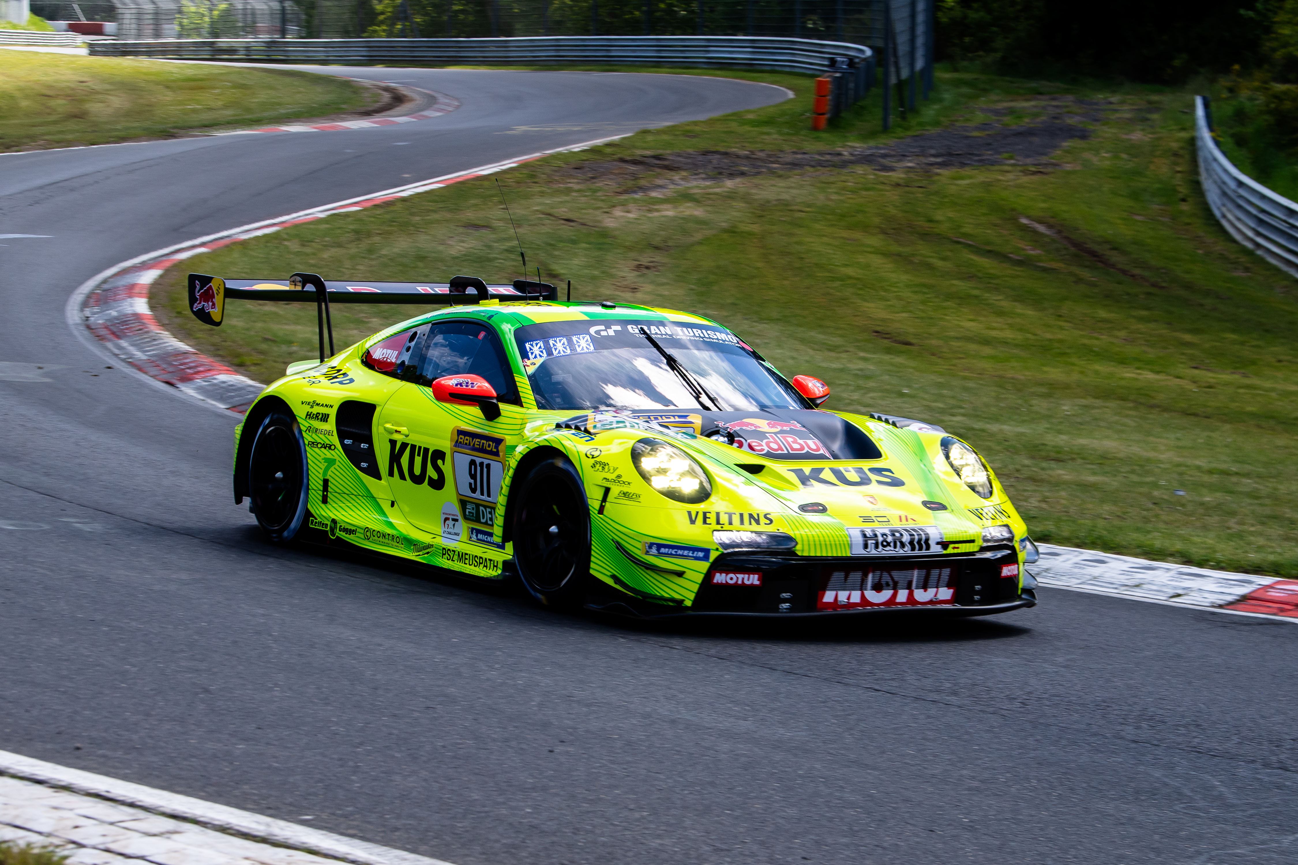 Manthey SP 9 PRO (IGTC) (#911) mit den Fahrern Kevin Estre (FRA), Ayhancan Güven (TUR), Thomas Preining (AUT). Der gelb-grüne Manthey Porsche 911 GT3 R (#911) mit KÜS-Beklebung fährt auf der Rennstrecke während des ADAC RAVENOL 24h Nürburgring GE Qualifying 1