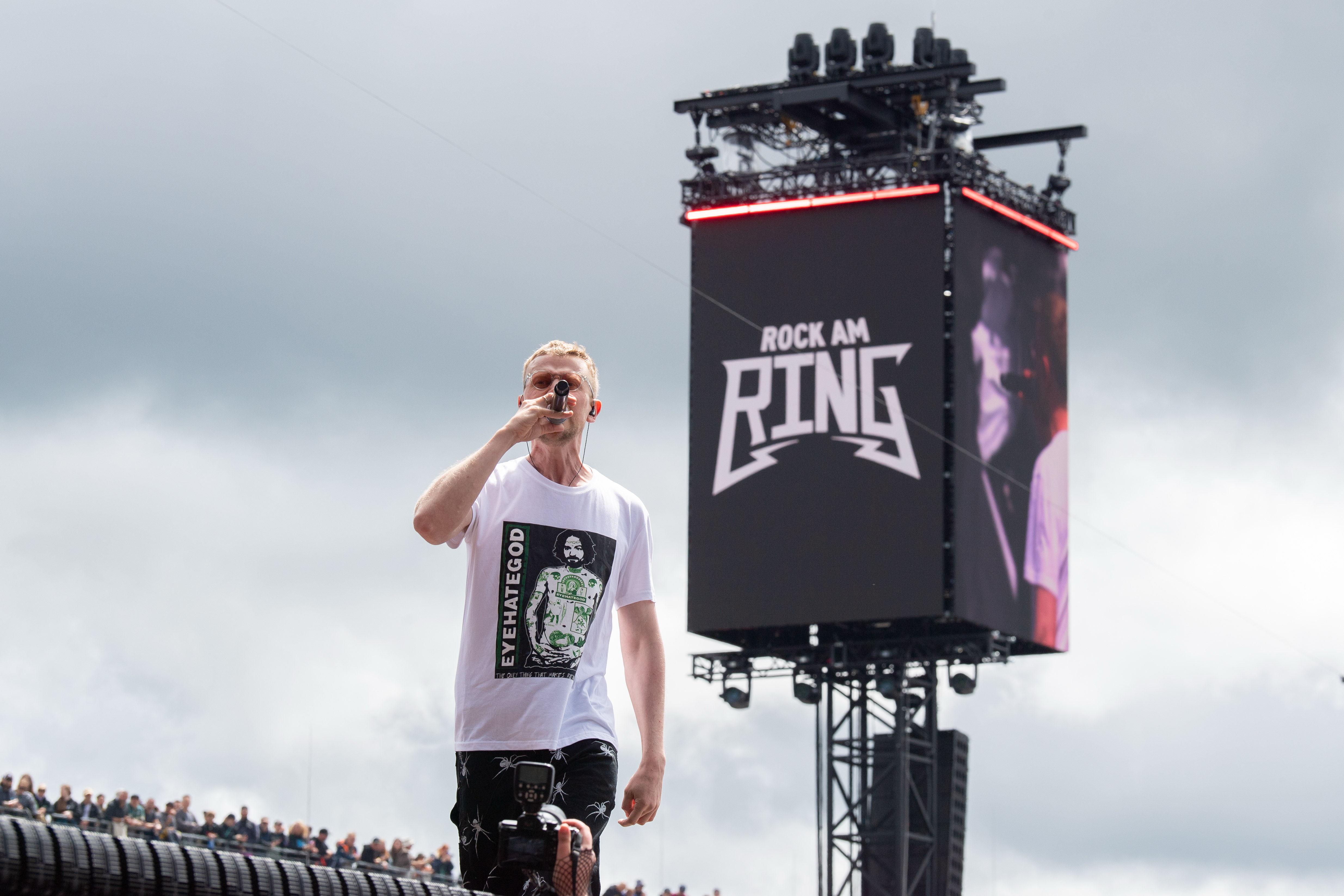 Sänger von Don Broco beim Rock am Ring Festival am Freitag, Nürburgring. Die Aufnahme zeigt die Bühnenperformance vor sichtbarem Publikum und einer großen Anzeige mit dem Festival-Logo.