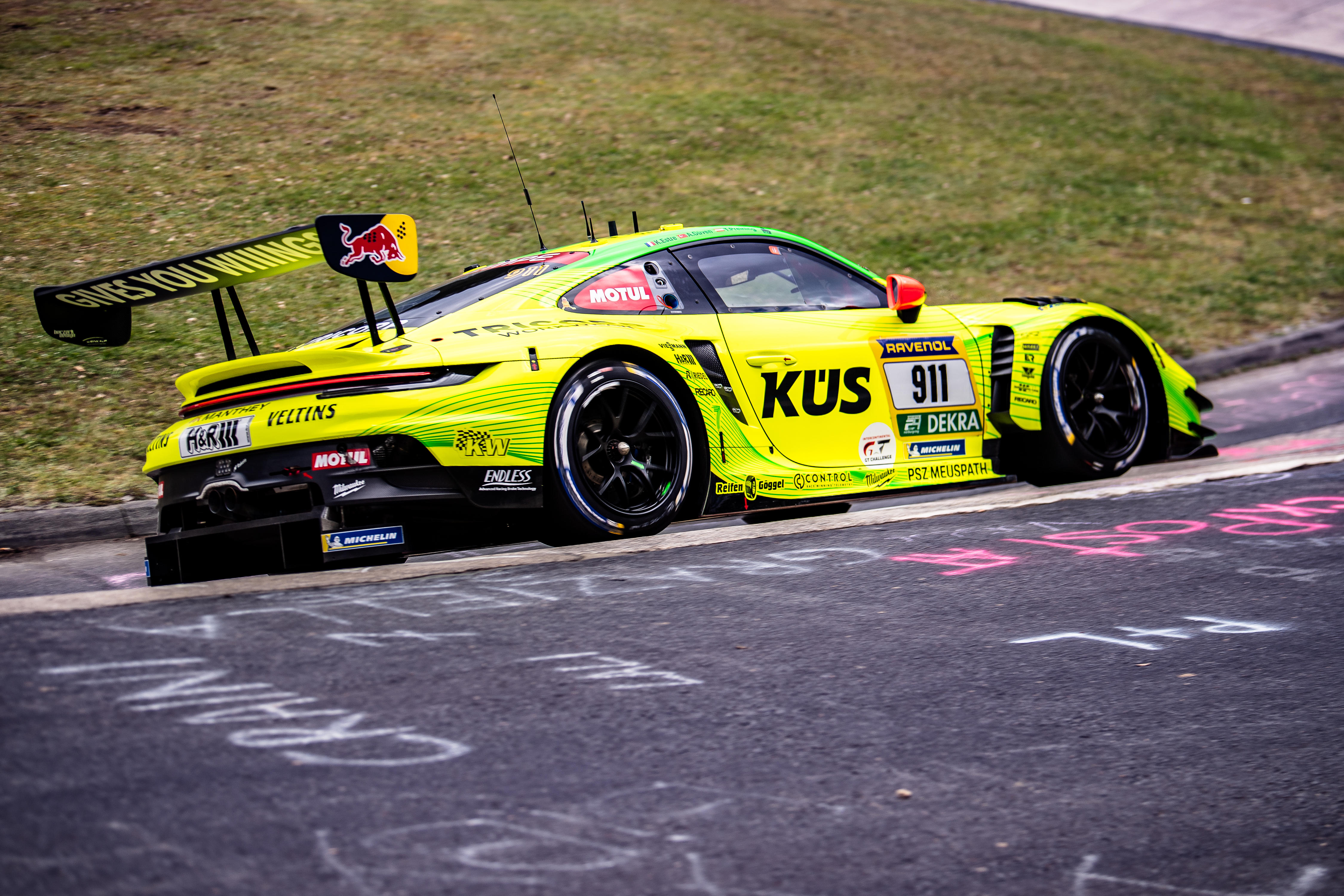 Manthey (#911) SP 9. Der gelb-grüne Porsche 911 GT3 R (#911) mit Sponsoren wie KÜS und Ravenol fährt auf der Rennstrecke am Nürburgring.