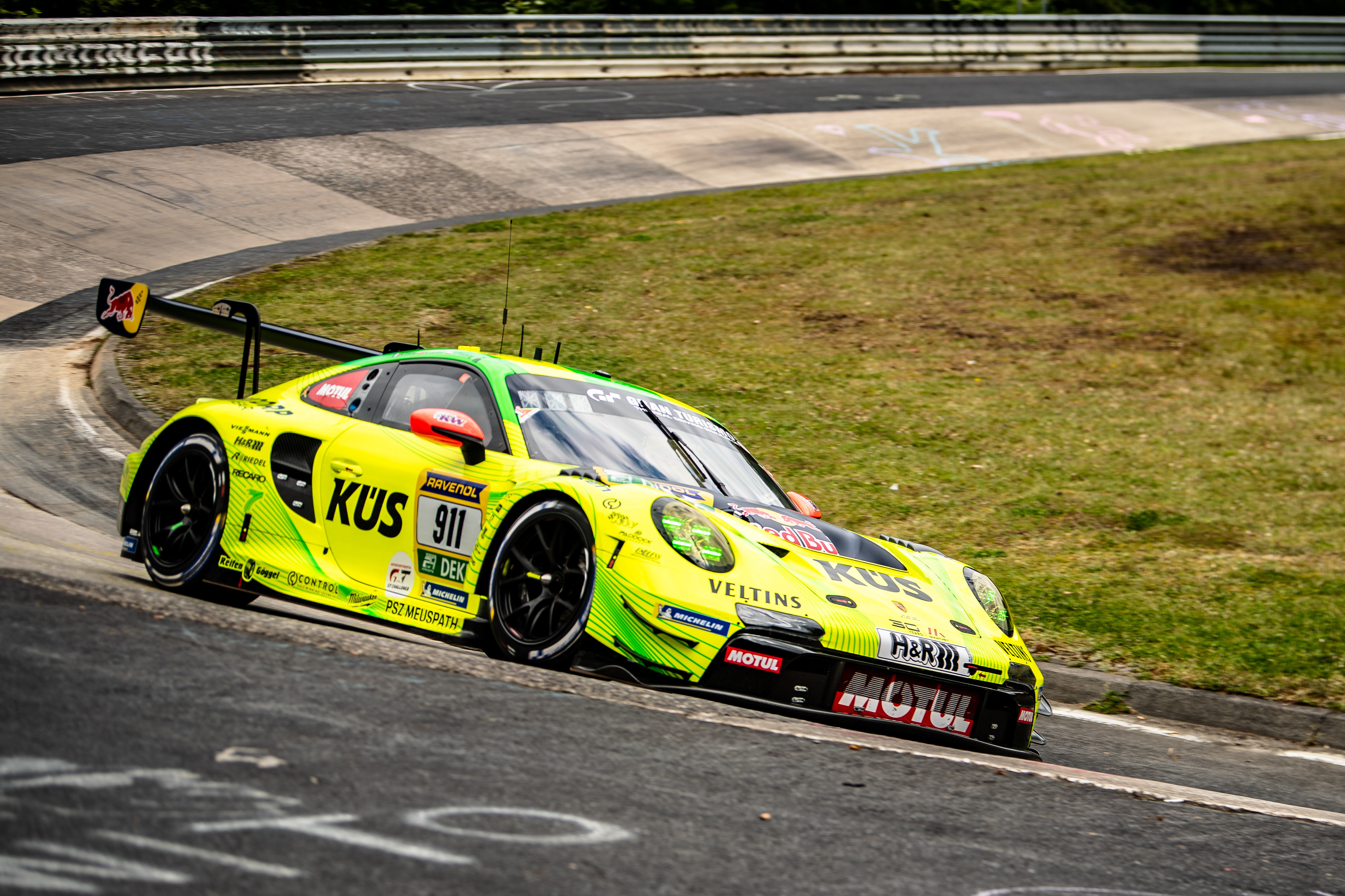 Manthey (#911) SP 9. Ein gelb-grün lackierter Porsche 911 GT3 R mit der Startnummer (911) fährt auf der kurvigen Nordschleife in einer Schikane.
